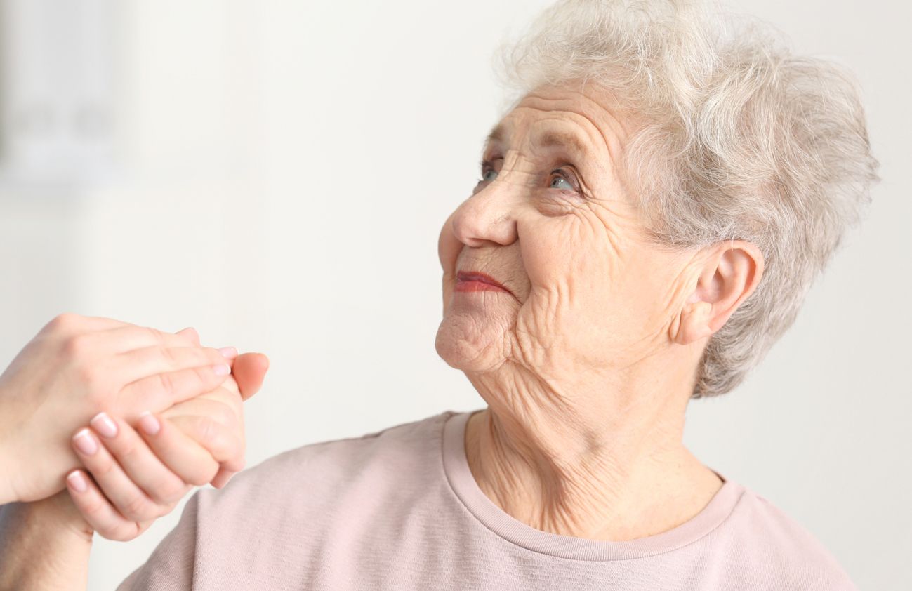 Eine Frau hält die Hand einer älteren Dame, was eine herzliche und fürsorgliche Geste der Verbundenheit darstellt.