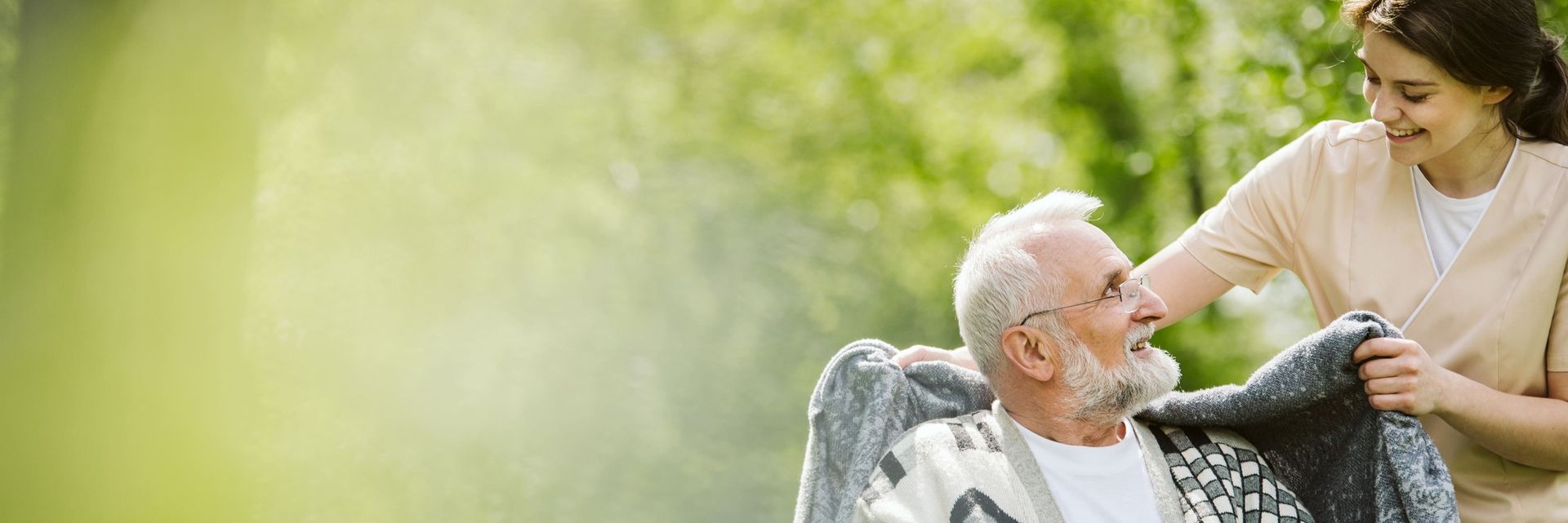 Pflegerin lächelt alten Mann an und legt ihm eine Decke um die Schultern