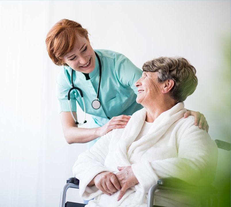 Pflegerin lächelt alte Frau im Rollstuhl an